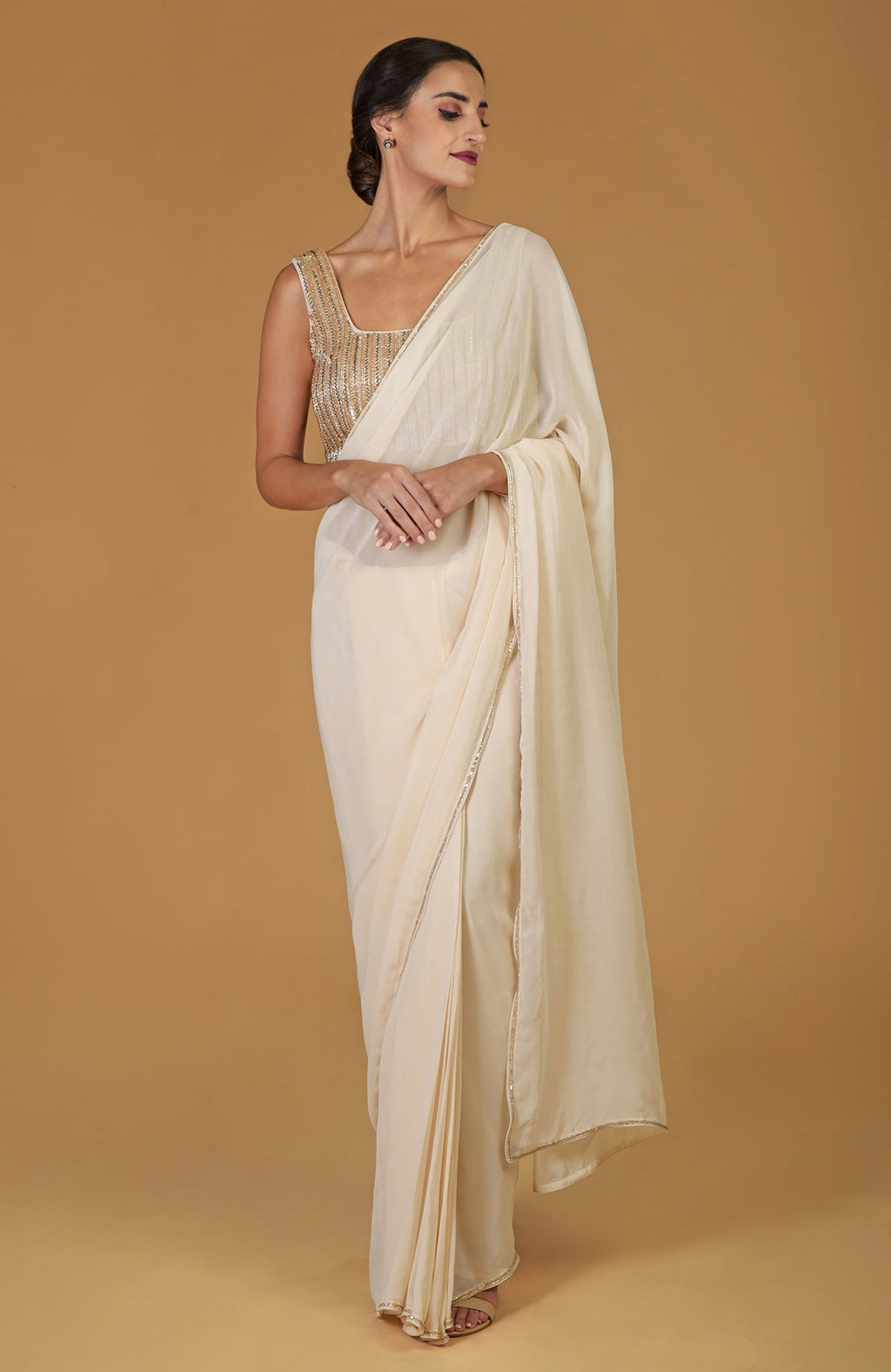 A woman models a champagne gold hand-embroidered saree and blouse.