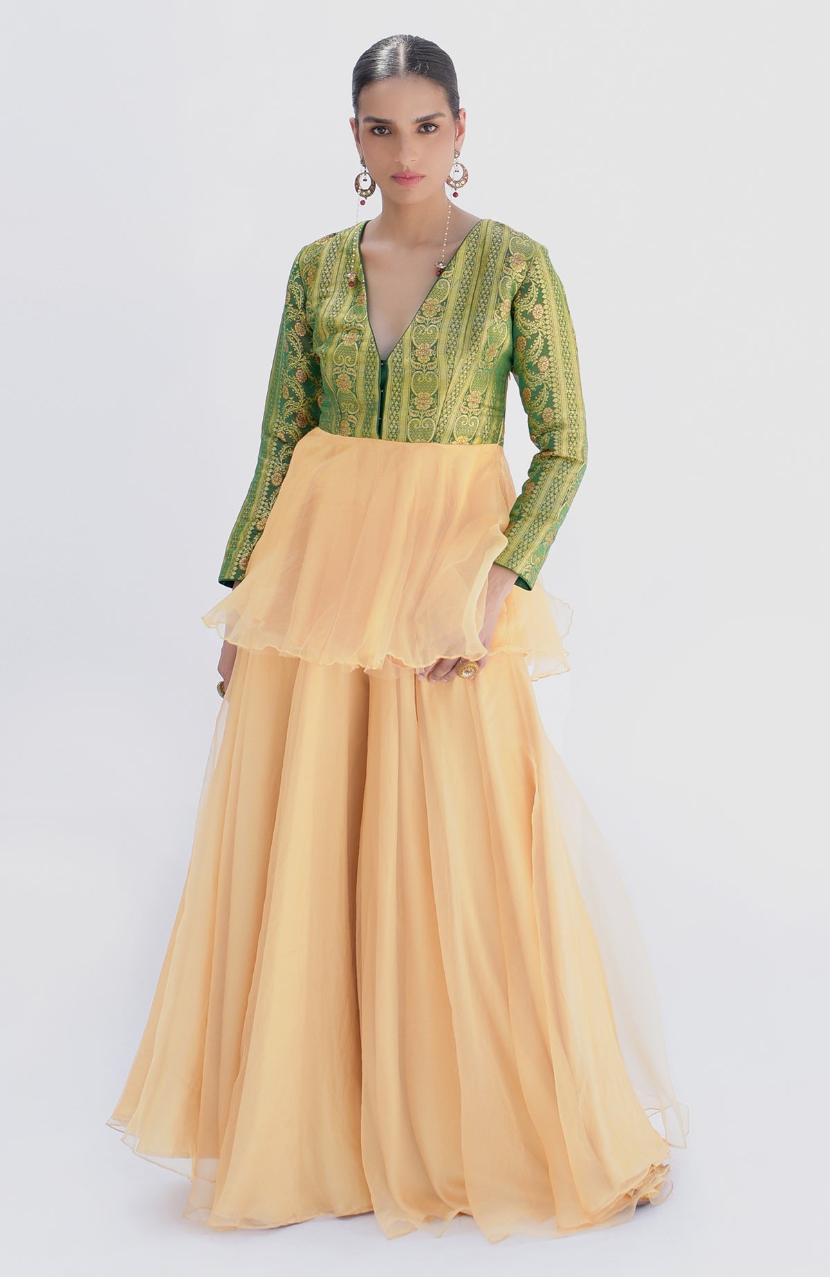A woman models a green Banarasi peplum top with a gold sharara.