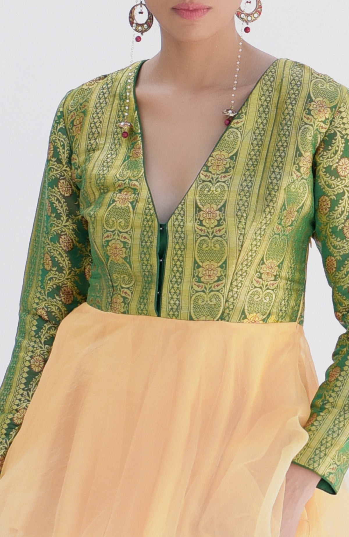 A woman wears a green and gold brocade peplum top with a light orange skirt.
