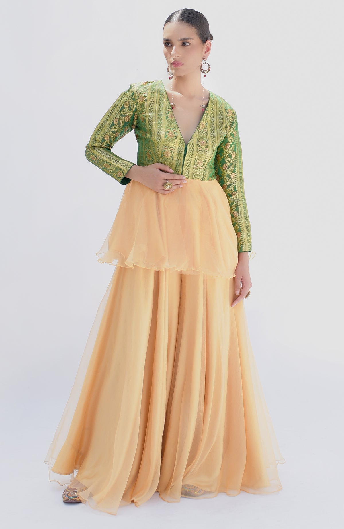 A model wears a green Banarasi peplum top with a gold sharara.