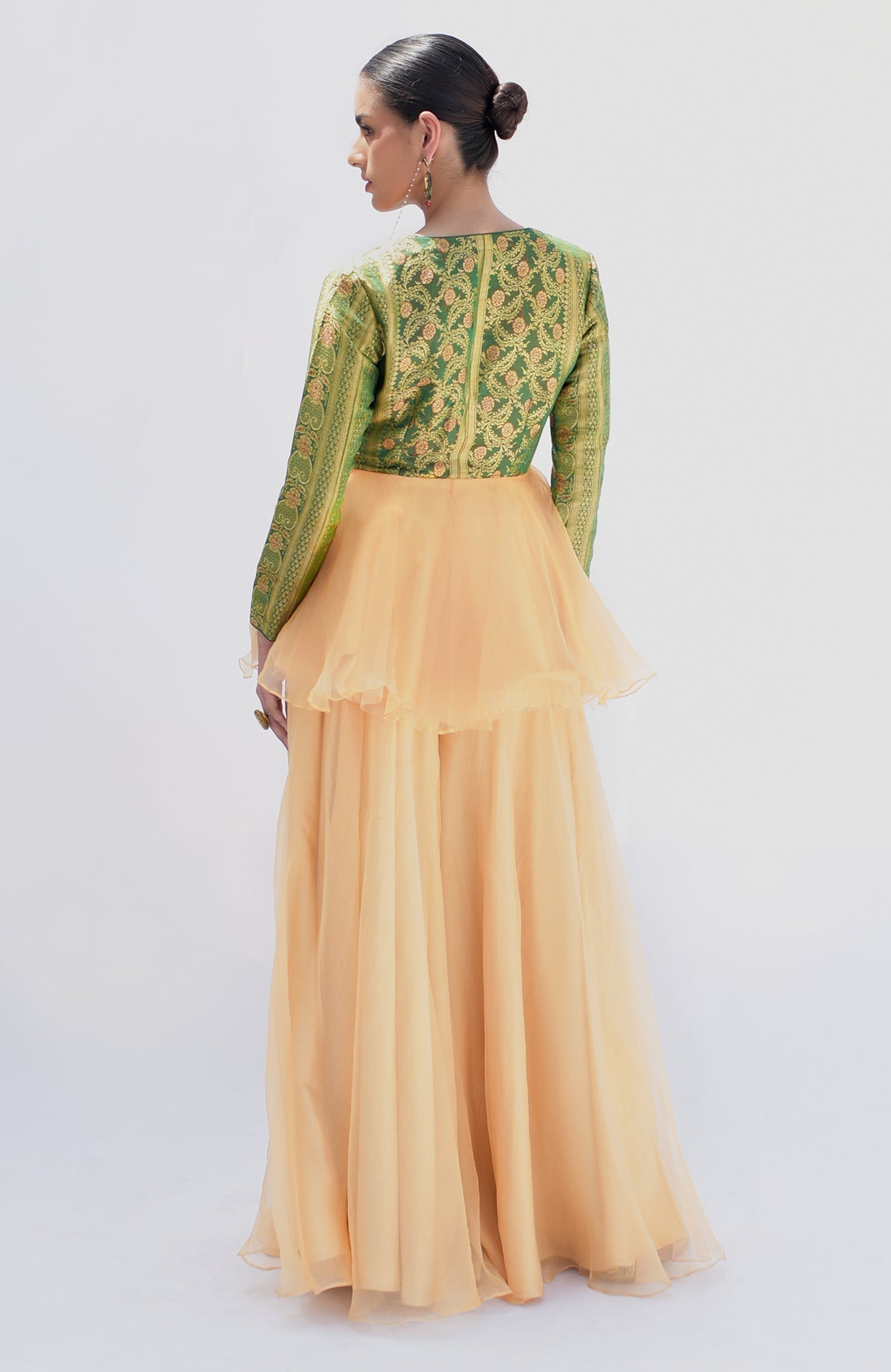 A woman models a green Banarasi peplum top with a gold sharara.