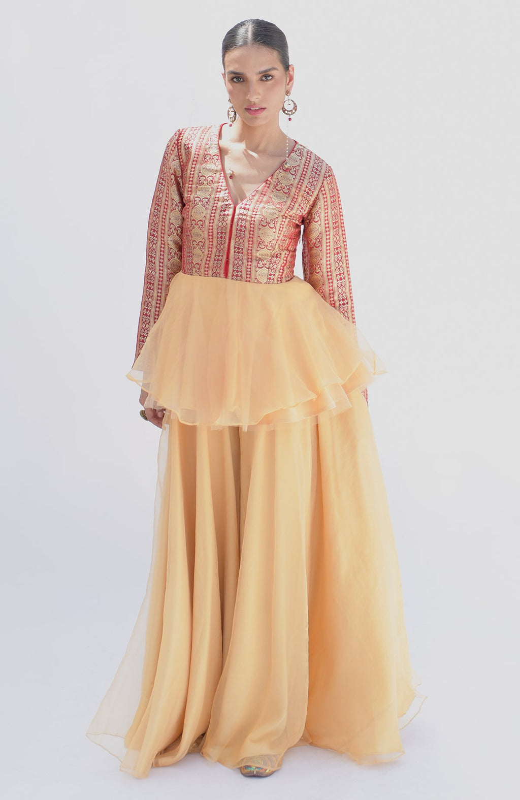A woman models a red and gold Banarasi peplum top with a gold sharara.