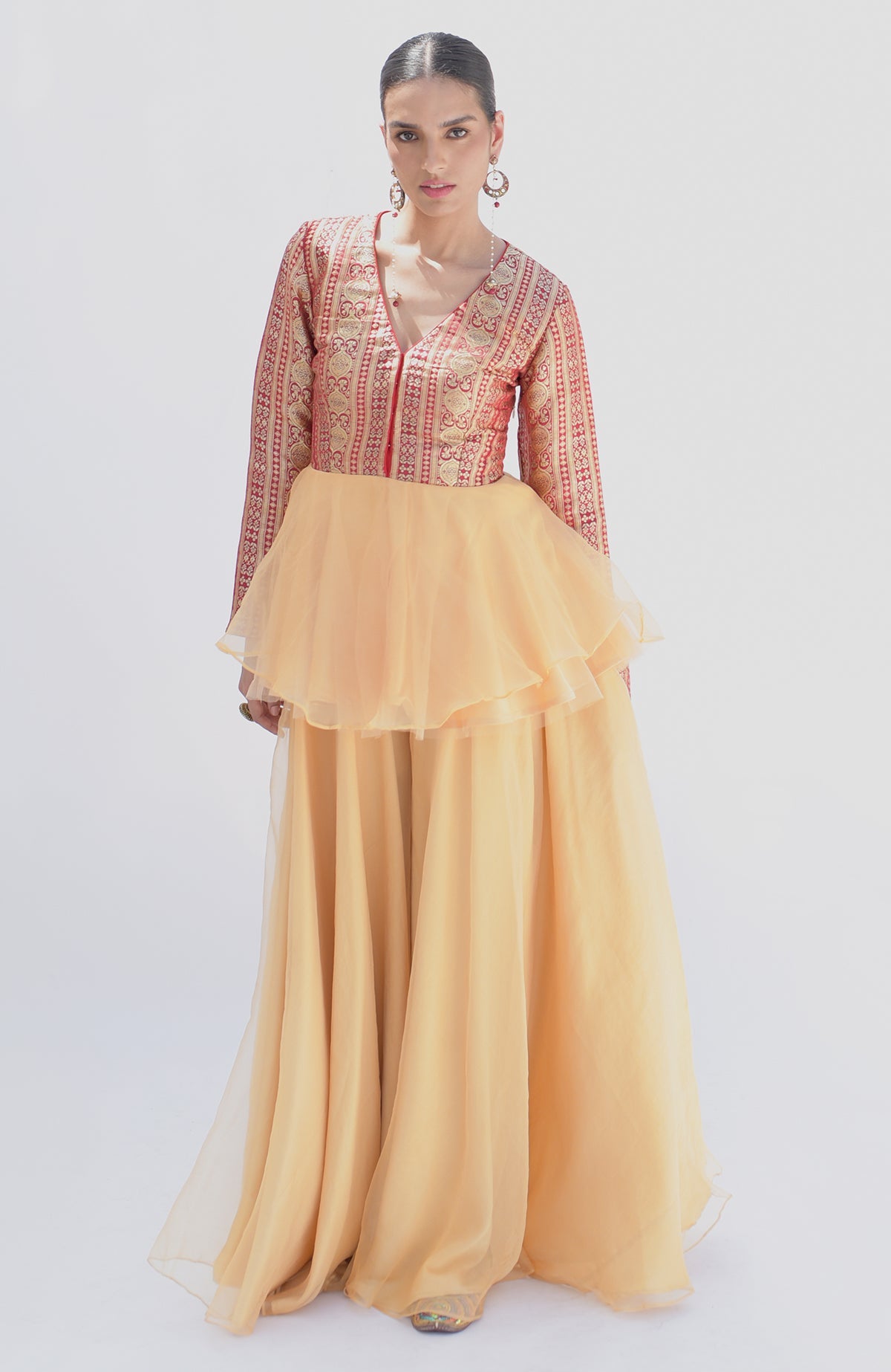 A woman models a red and gold Banarasi peplum top with a gold sharara.
