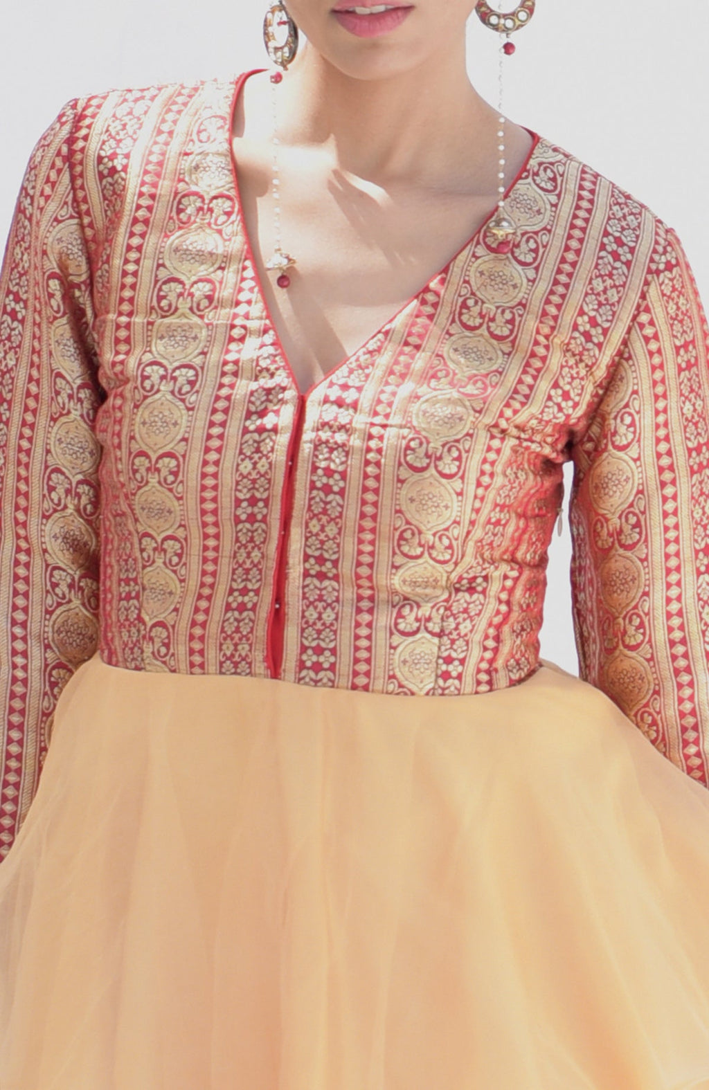 A woman wears a red and gold patterned peplum top with a light gold skirt.