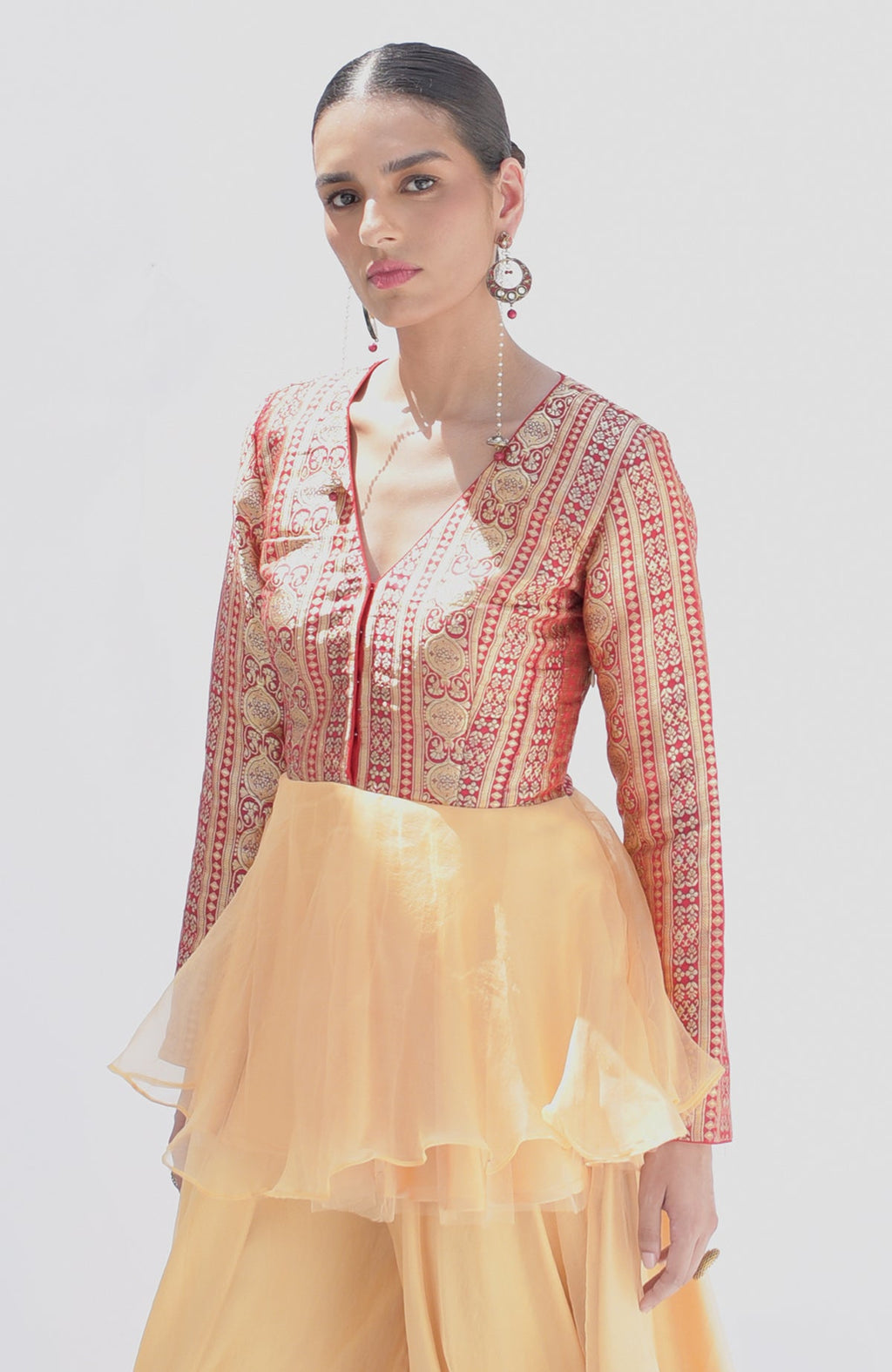 A woman models a red and gold Banarasi peplum top with a gold sharara.
