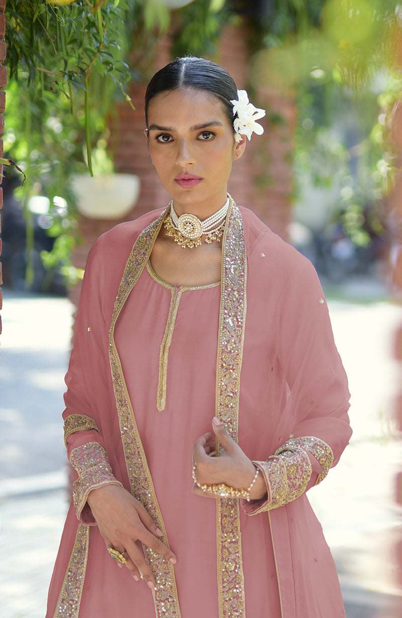 Woman in a pink kurta set with gold embroidery and a pearl choker.
