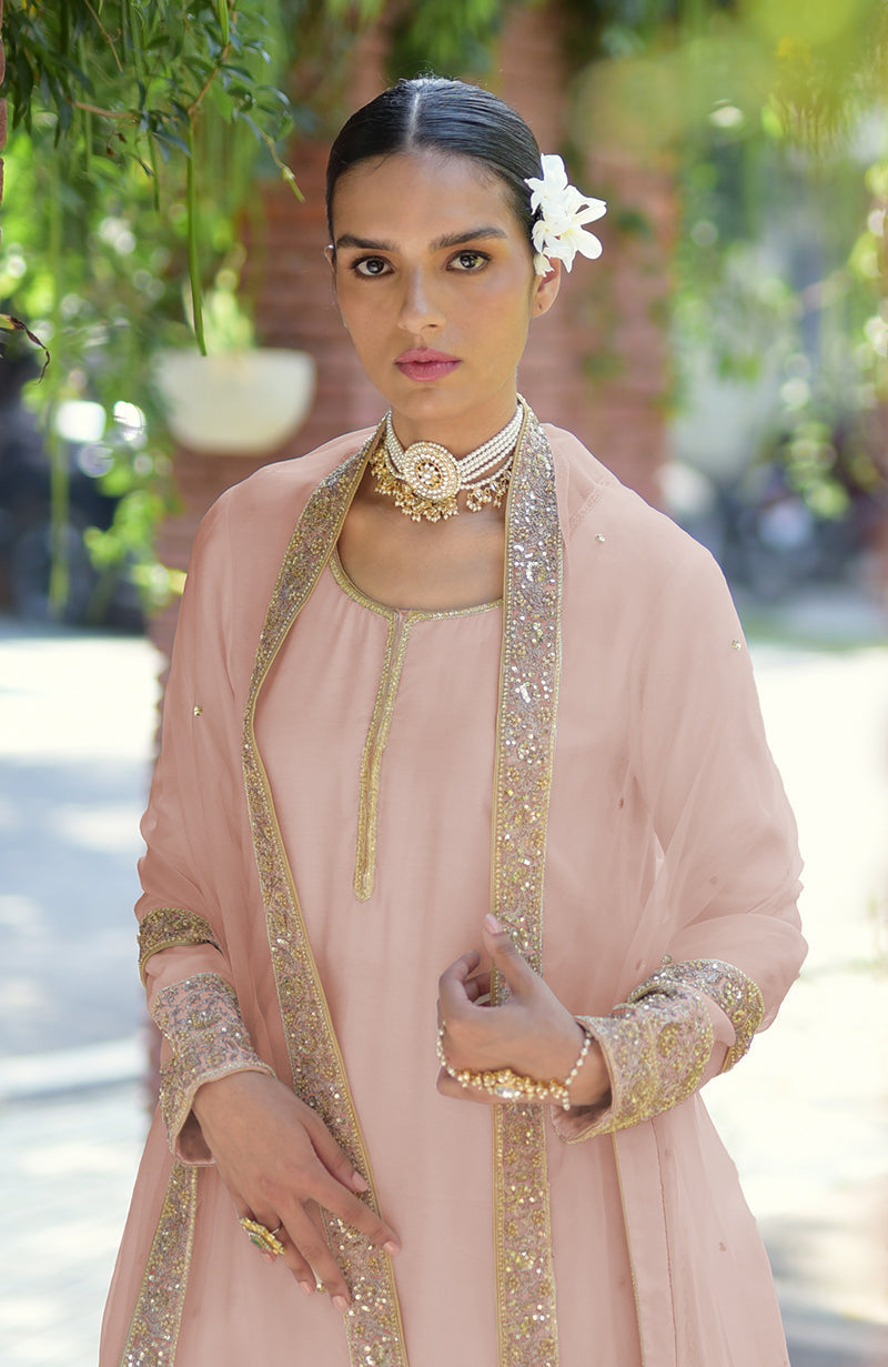A woman in a light pink kurta set with gold embroidery and a pearl choker.