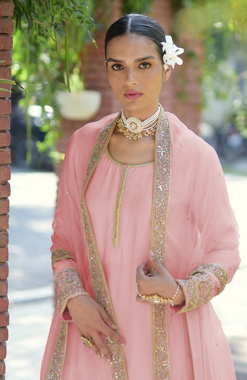 A woman in a pink kurta set with gold embroidery and a pearl choker.