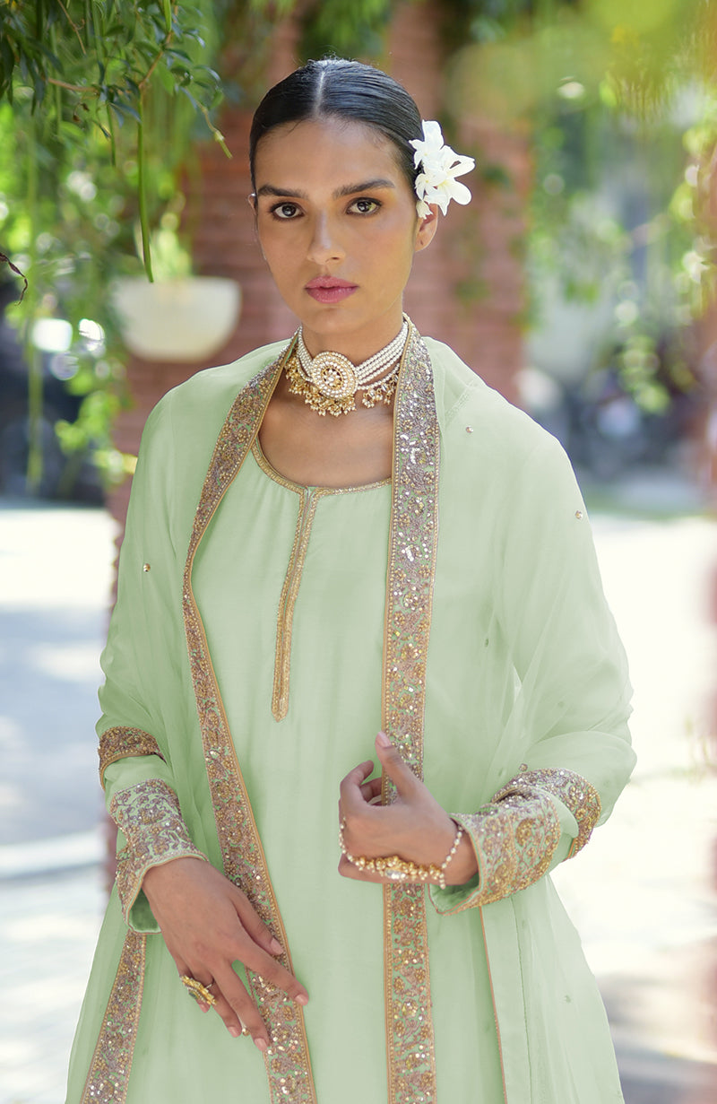 A woman in a light green kurta set with gold embroidery and a pearl choker.