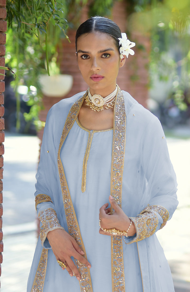 A woman in a light blue kurta set with gold embroidery and a pearl choker.